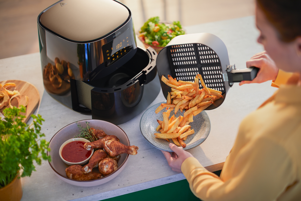 Woman using Philips Essential Airfryer XL to cook fried chicken and chips